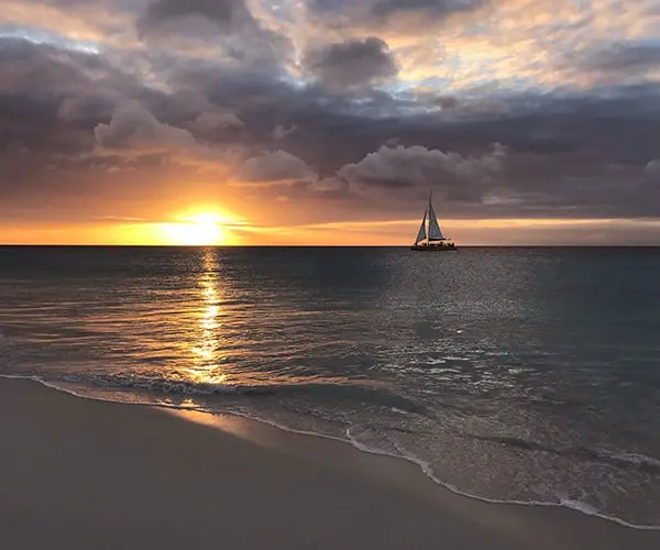 Sunset on Eagle Beach in Aruba looking over the water with a sailboat in the distance