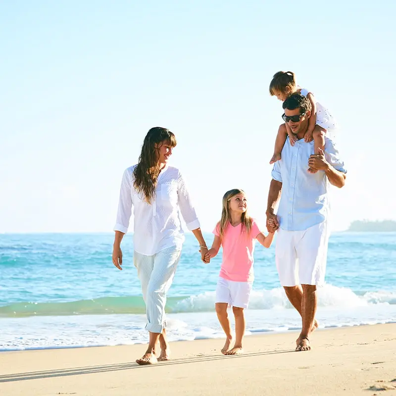 A family of 4 walks hand in hand on the beach smiling