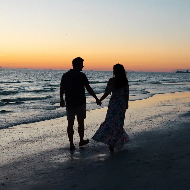 A couple walks hand in hand down the beach in silhouette at sunset after their vow renewal ceremony