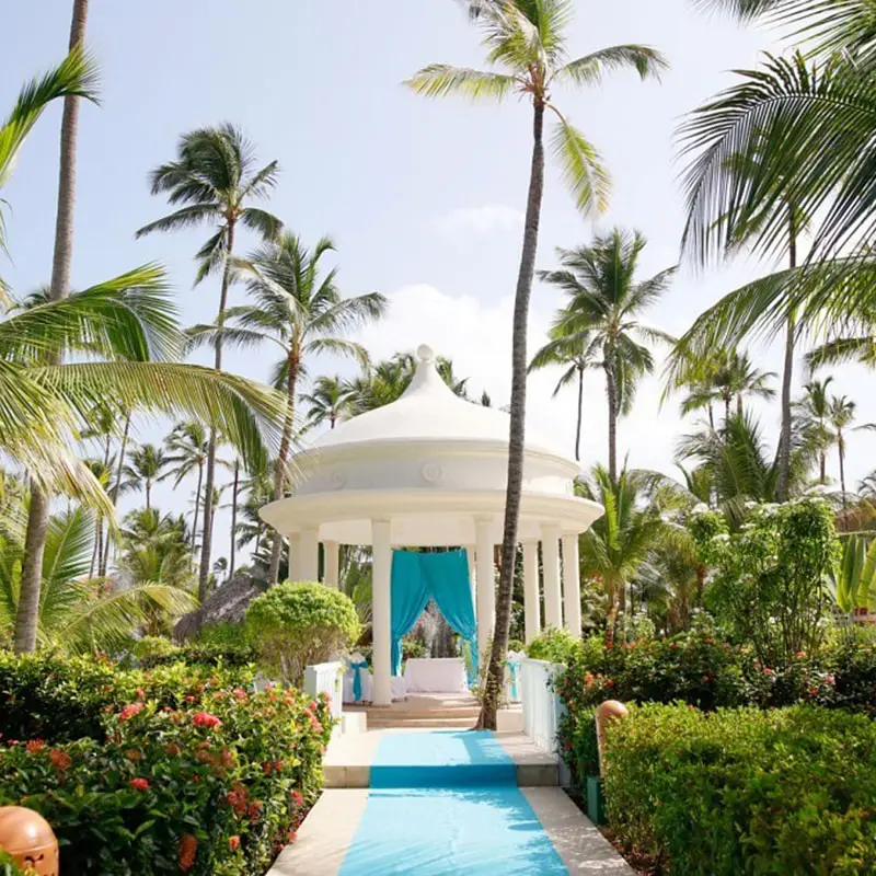 An elegant gazebo is decorated for a wedding set in a garden with palm trees