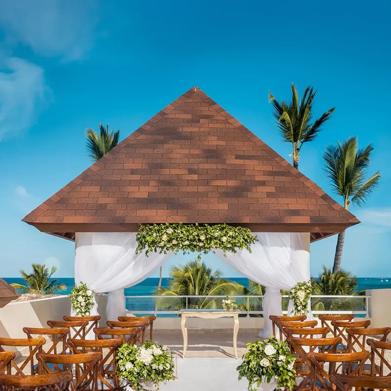 A roofed gazebo is decorated for a wedding, with elegant chairs in rows on either side of the aisle.
