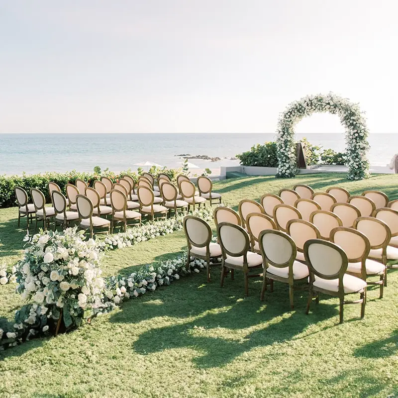 A flower-covered arch and elegant chairs lay the scene for a garden wedding near the ocean