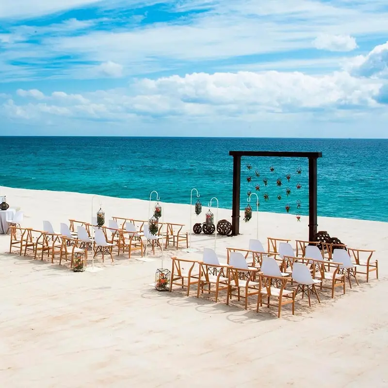 Turquoise blue water and white sand beach is the setting for a dark wooded wedding altar and chairs