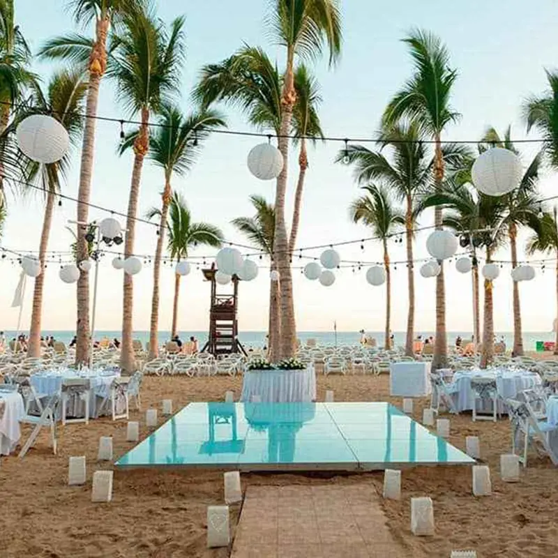 A unique beach wedding set up with a raise glass floor for the ceremony and reception tables spread out around it.