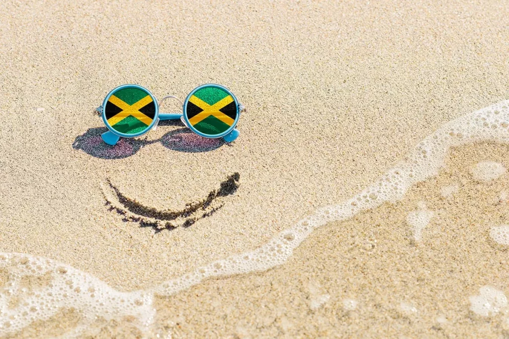 Sunglasses with Jamaican flags in the lenses sits on a white sand beach