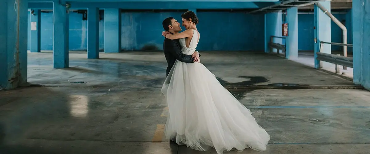 An urban chic scene wherein a wedding couple embraces in a bright blue parking lot